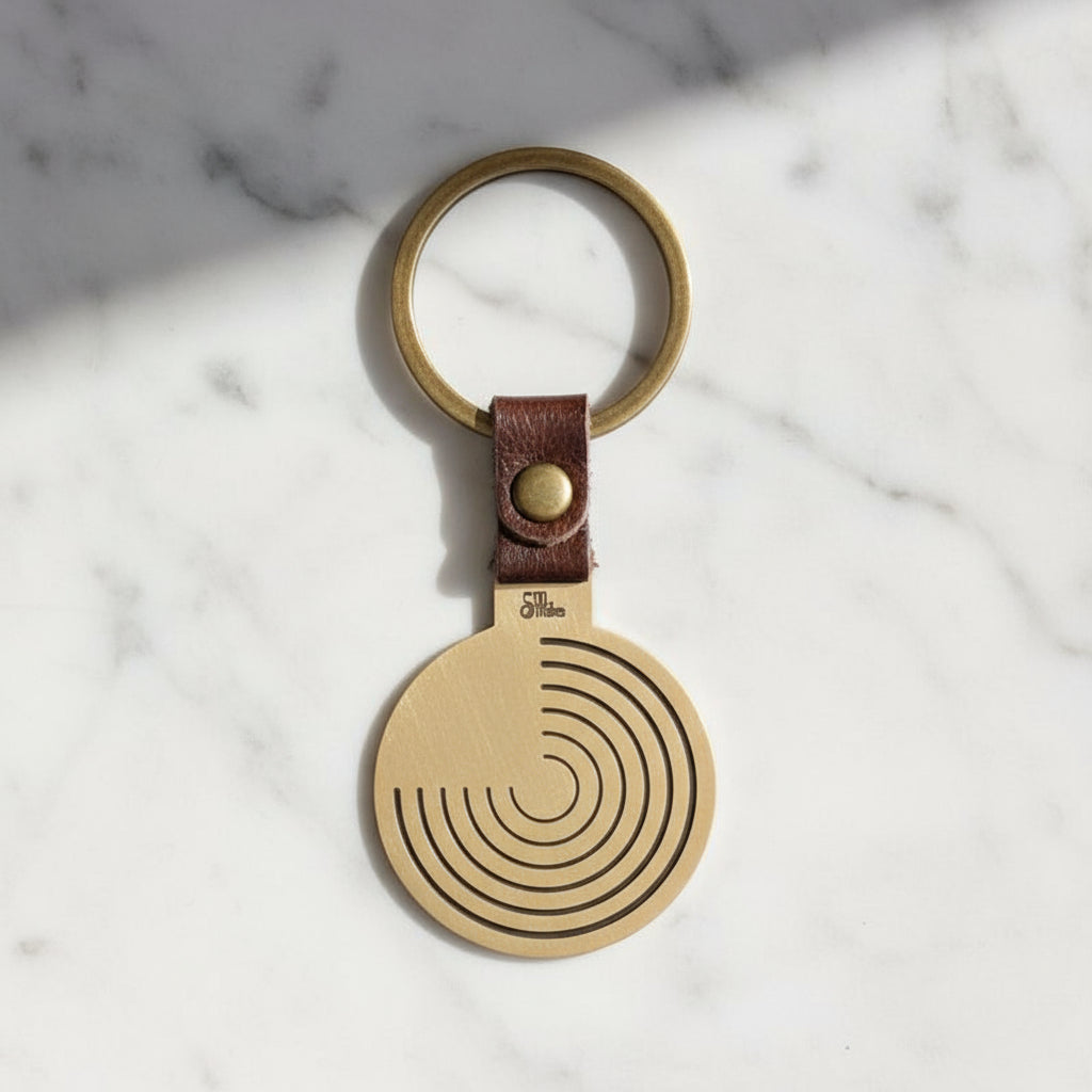 A brass keychain with concentric circle pattern and a leather strap.